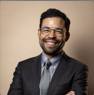 A photo of Elijah Hutchinson smiling, wearing a formal suit.